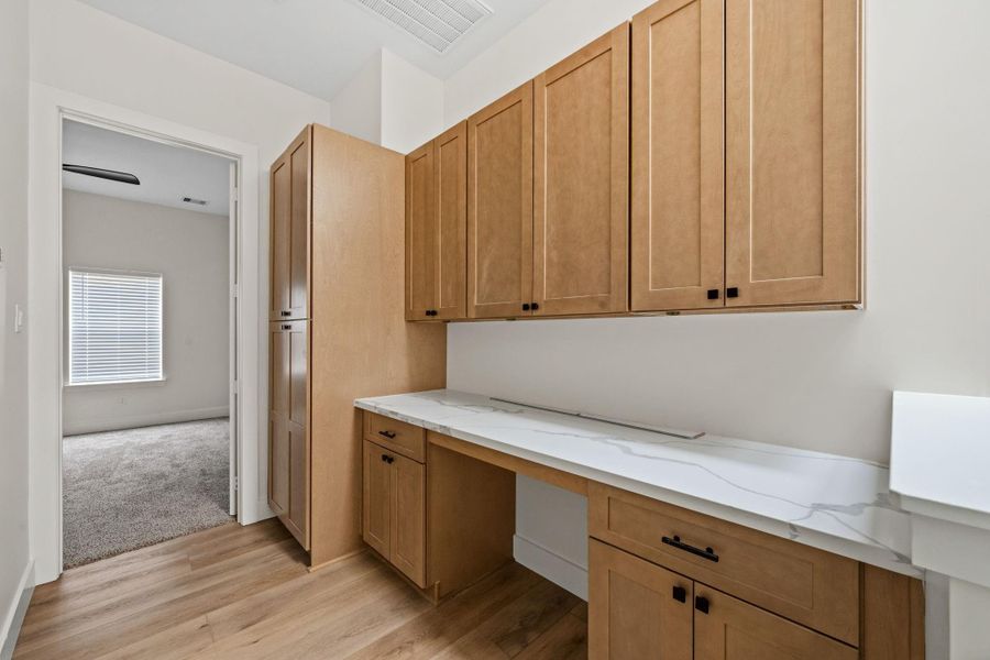 Elegant hallway with ample storage in sleek wooden cabinets and a polished countertop, leading to a cozy carpeted room with natural light.