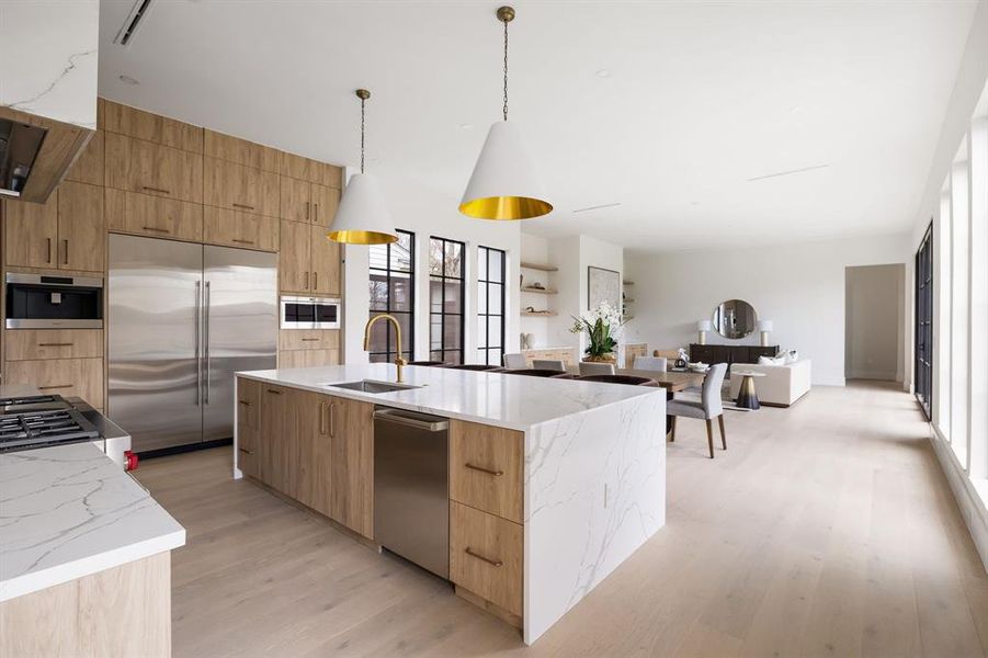 Kitchen with a sink, stainless steel built in refrigerator, modern cabinets, decorative light fixtures, and an island with sink