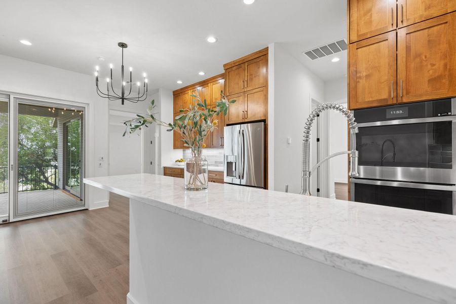 Kitchen featuring appliances with stainless steel finishes, wood finished floors, light stone countertops, recessed lighting, and brown cabinetry Kitchen featuring appliances with stainless steel finishes, wood finished floors, light stone countertops, recessed lighting, and brown cabinetry