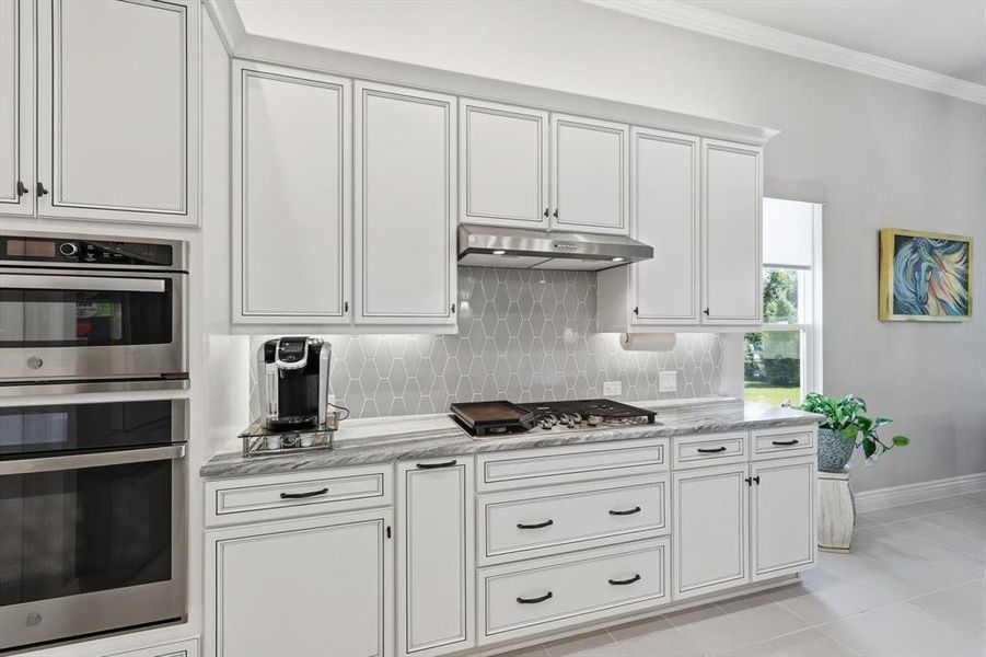 Modern kitchen featuring white cabinetry with dark hardware, stainless steel built-in appliances, a gas cooktop, and a honeycomb tile backsplash