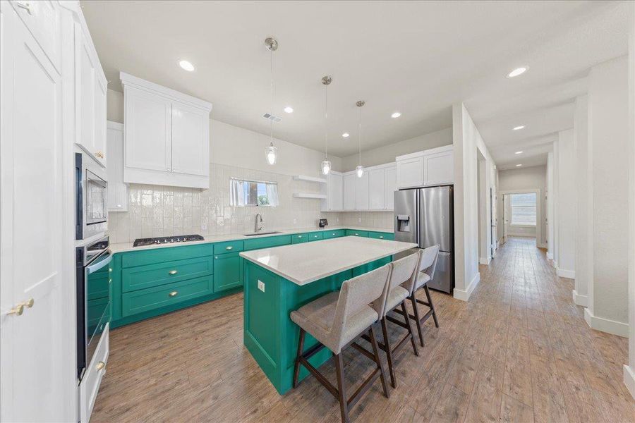 Kitchen featuring stainless steel appliances, a kitchen island, white cabinetry, a breakfast bar, and light wood finished floors Kitchen featuring stainless steel appliances, a kitchen island, white cabinetry, a breakfast bar, and light wood finished floors