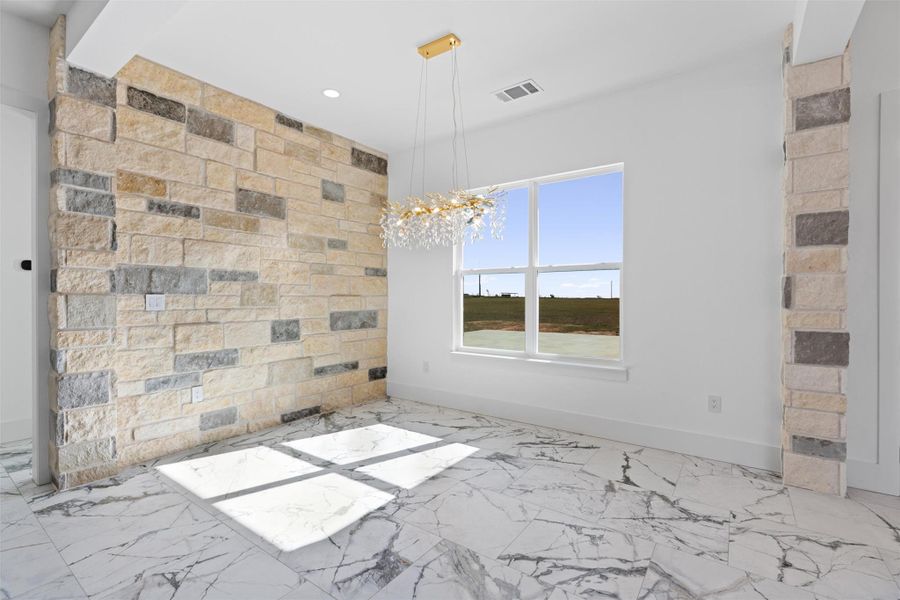 A striking stone accent wall enhances this room, featuring elegant tile flooring and an ornate chandelier. A striking stone accent wall enhances this room, featuring elegant tile flooring and an ornate chandelier.