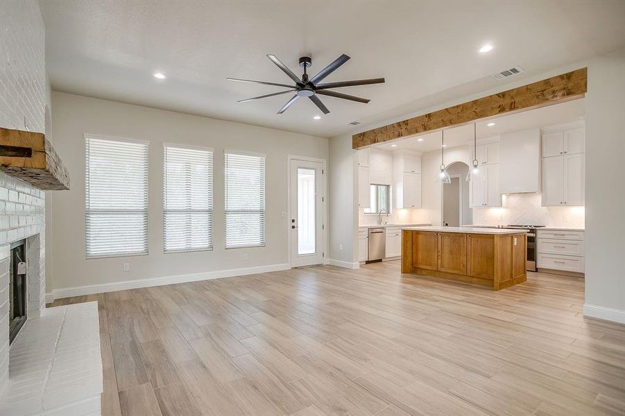 Kitchen with light countertops, light wood finished floors, a fireplace, decorative backsplash, and a ceiling fan Kitchen with light countertops, light wood finished floors, a fireplace, decorative backsplash, and a ceiling fan