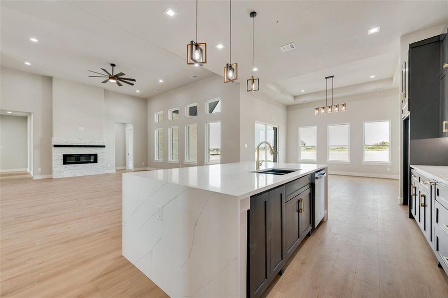 Kitchen featuring light hardwood / wood-style floors, sink, a stone fireplace, and a kitchen island with sink