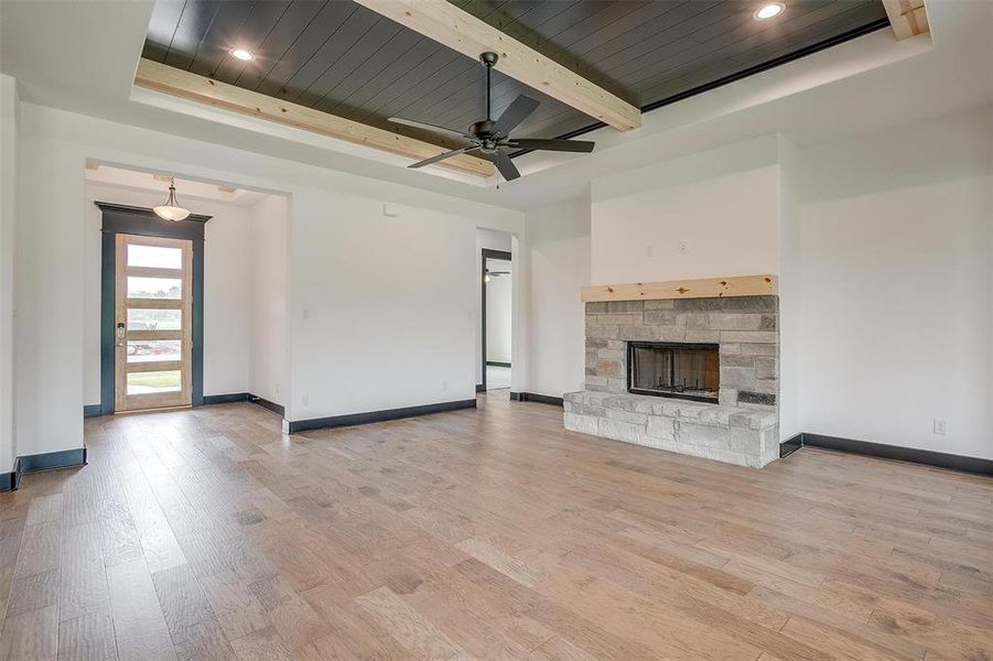 Unfurnished living room with a stone fireplace, light hardwood / wood-style flooring, beamed ceiling, and wood ceiling