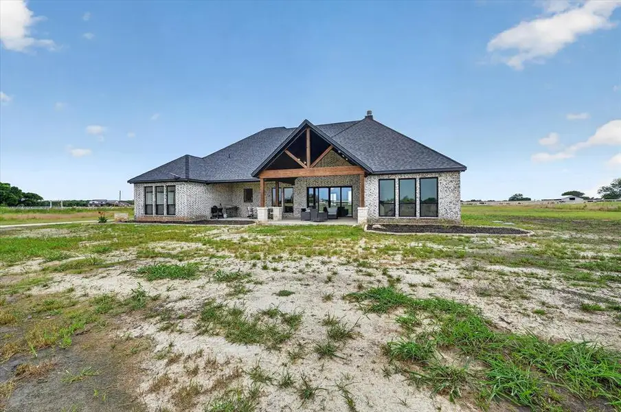 Rear exterior showcasing a covered patio with exposed wood beams, a stone-faced fireplace, and expansive glass doors
