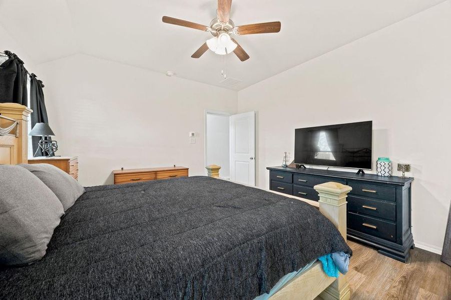 Vaulted ceiling bedroom with wood-finish flooring, a ceiling fan with light fixture, and neutral wall tones Vaulted ceiling bedroom with wood-finish flooring, a ceiling fan with light fixture, and neutral wall tones