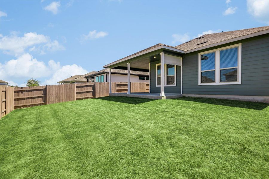 A manicured lawn spans the backyard beside a covered concrete patio and wooden privacy fencing. A manicured lawn spans the backyard beside a covered concrete patio and wooden privacy fencing.