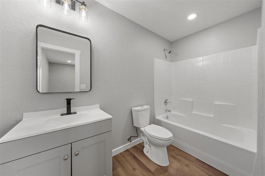 Full bathroom featuring wood finished floors, vanity, washtub / shower combination, and a textured wall Full bathroom featuring wood finished floors, vanity, washtub / shower combination, and a textured wall