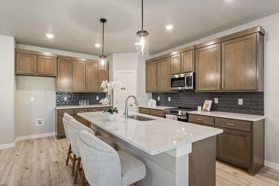 Kitchen featuring decorative light fixtures, light stone counters, a breakfast bar, light wood-style floors, and appliances with stainless steel finishes Kitchen featuring decorative light fixtures, light stone counters, a breakfast bar, light wood-style floors, and appliances with stainless steel finishes