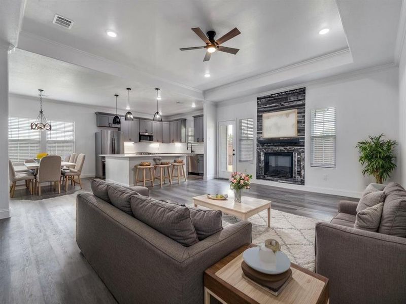 Living area featuring plenty of natural light, wood finished floors, a fireplace, crown molding, and a ceiling fan Living area featuring plenty of natural light, wood finished floors, a fireplace, crown molding, and a ceiling fan
