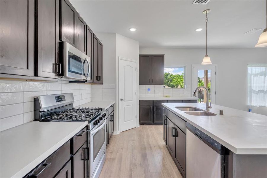 Kitchen with tasteful backsplash, light hardwood / wood-style floors, hanging light fixtures, appliances with stainless steel finishes, and sink