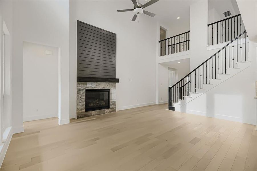 Unfurnished living room featuring a high ceiling, light wood finished floors, a ceiling fan, and a tiled fireplace