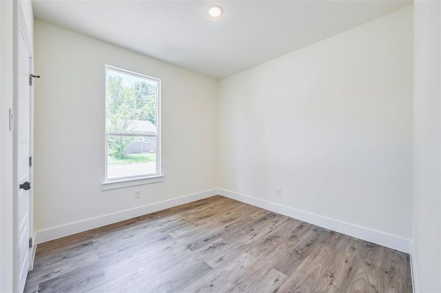 Room featuring wood-finish flooring, a single window with white trim, and a recessed ceiling light Room featuring wood-finish flooring, a single window with white trim, and a recessed ceiling light