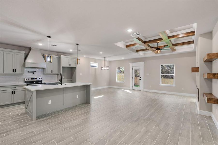 Kitchen with custom exhaust hood, stainless steel range with electric cooktop, beamed ceiling, coffered ceiling, and a kitchen island with sink