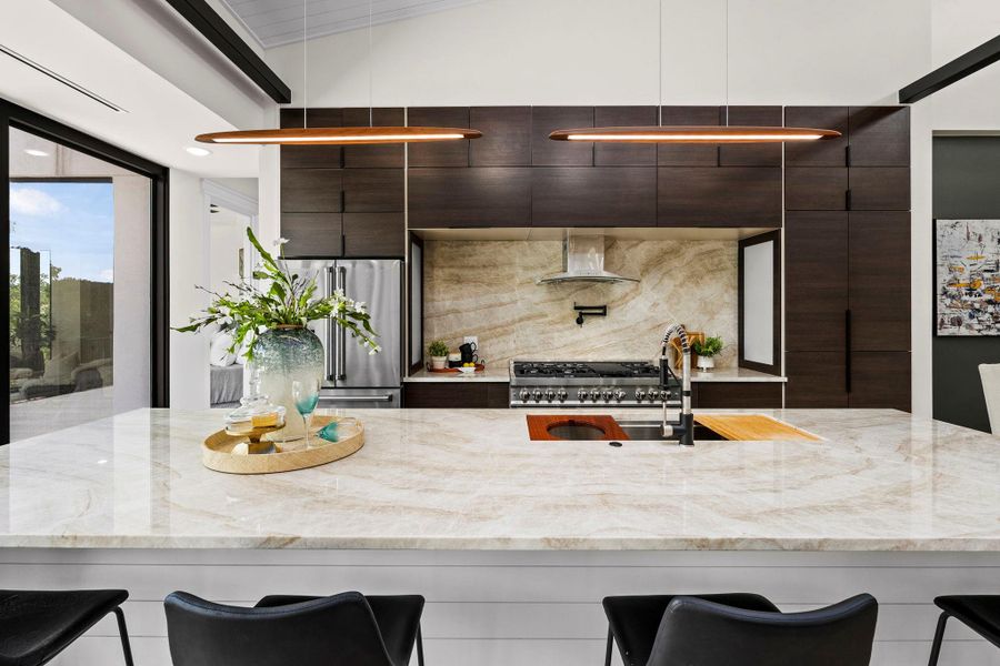 Kitchen with a breakfast bar, dark wood finish cabinets, modern cabinets, and light stone countertops