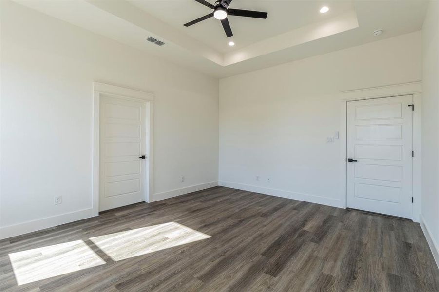 Empty room featuring ceiling fan, a tray ceiling, and dark wood-type flooring