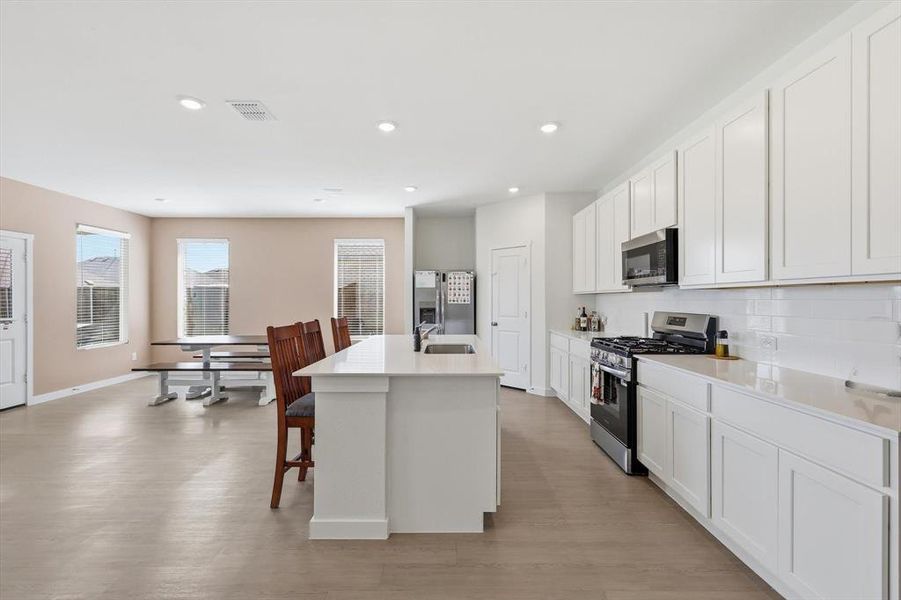 Open-concept kitchen featuring an eat-in island, white cabinetry, a gas range, stainless steel appliances, and a subway tile backsplash Open-concept kitchen featuring an eat-in island, white cabinetry, a gas range, stainless steel appliances, and a subway tile backsplash