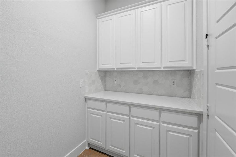 This space features extensive white cabinetry, a light-toned countertop, and a decorative tile backsplash