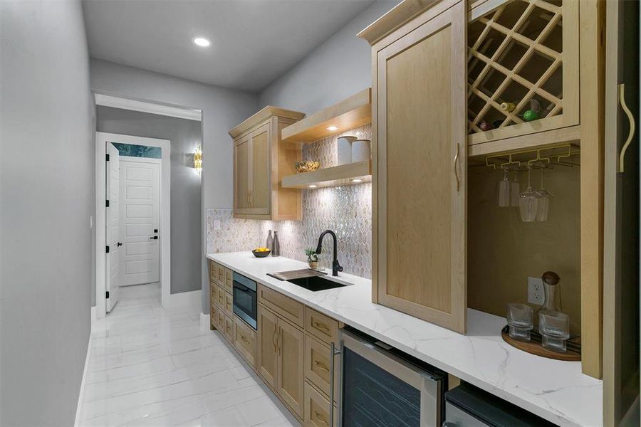 Kitchen featuring sink, light brown cabinets, beverage cooler, tasteful backsplash, and stainless steel microwave