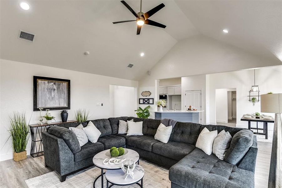 Living area with high vaulted ceiling, visible vents, ceiling fan, and light wood finished floors