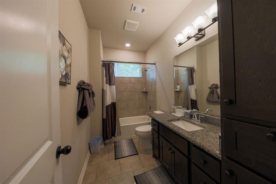 This is a modern bathroom featuring a double sink vanity with granite countertops, a full-size bathtub with a tiled shower area, and elegant lighting fixtures. The space is well-organized with ample storage, neutral tones, and a clean, contemporary design.