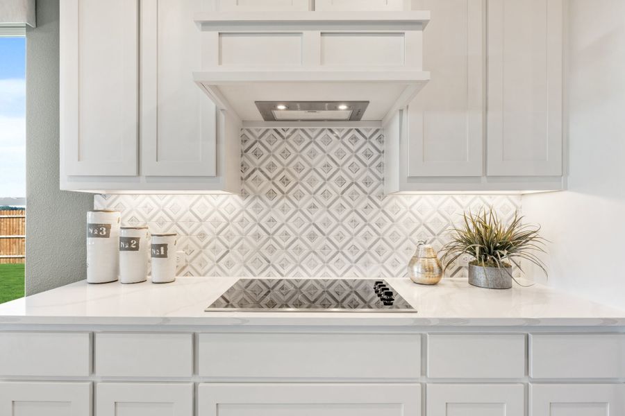 Kitchen cooktop area with white cabinets, geometric tile backsplash, and built-in range hood