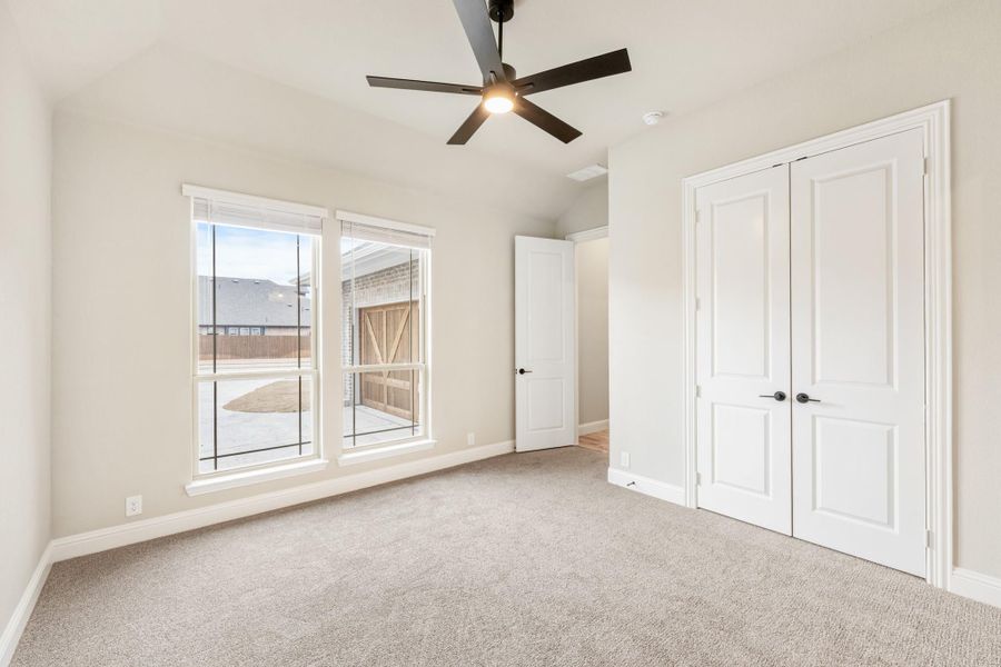 Empty bedroom with carpet, ceiling fan, double closet doors, and a window overlooking the backyard Empty bedroom with carpet, ceiling fan, double closet doors, and a window overlooking the backyard