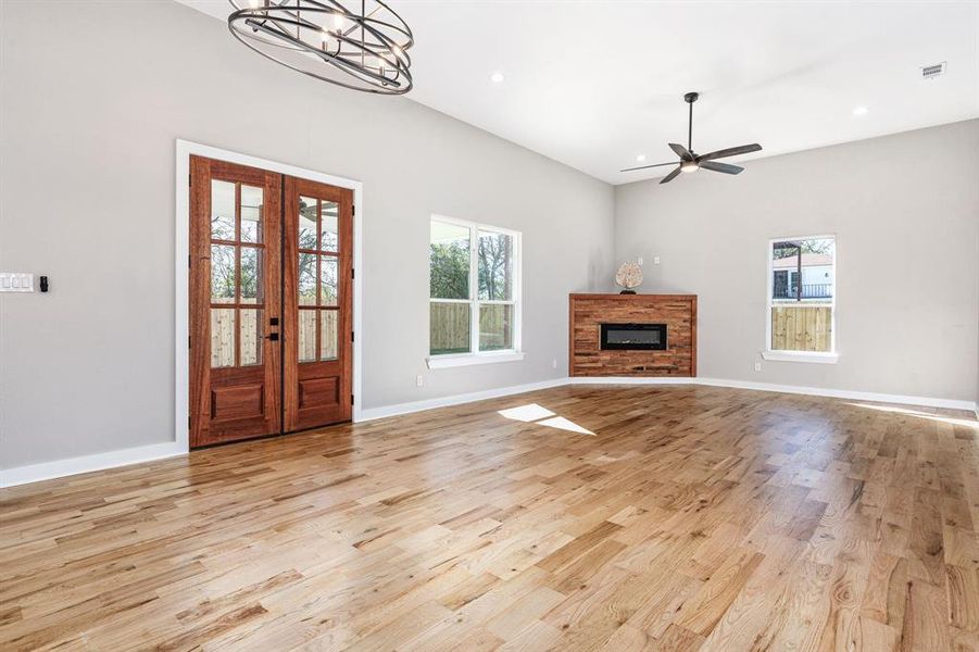 Unfurnished living room with ceiling fan with notable chandelier and light hardwood / wood-style flooring