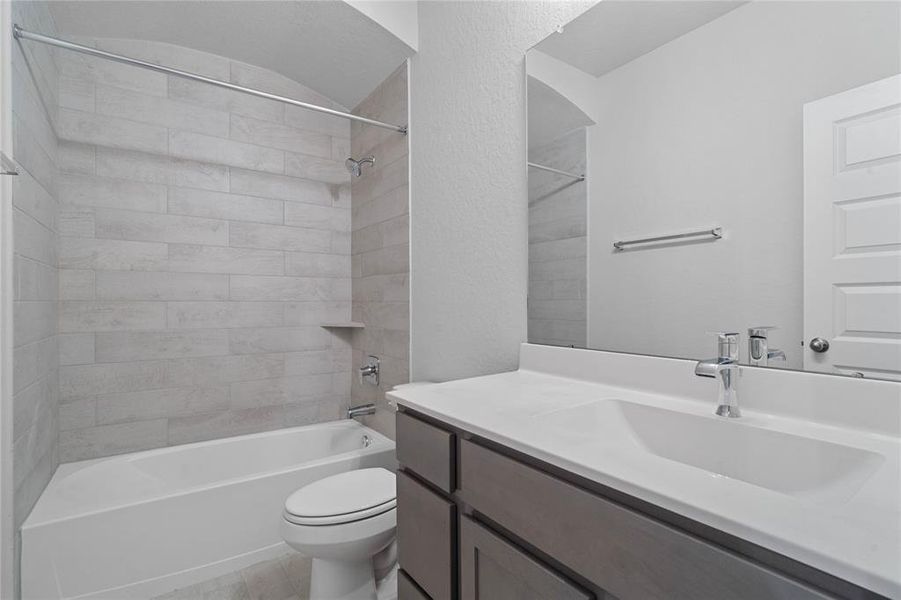 Secondary bathroom features light countertops and stained cabinets, custom paint, shower/tub combo with tile surround, large mirror, tile floors, sleek fixtures and modern finishes, plenty of space to accommodate any visiting family or guests.