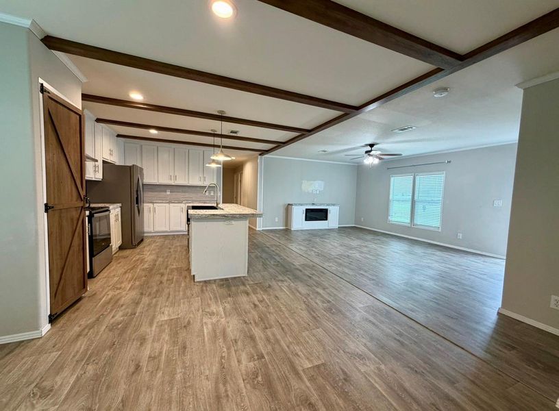 Open-concept living space with wood-finish flooring, exposed ceiling beams, recessed lighting, and a kitchen island with pendant lighting