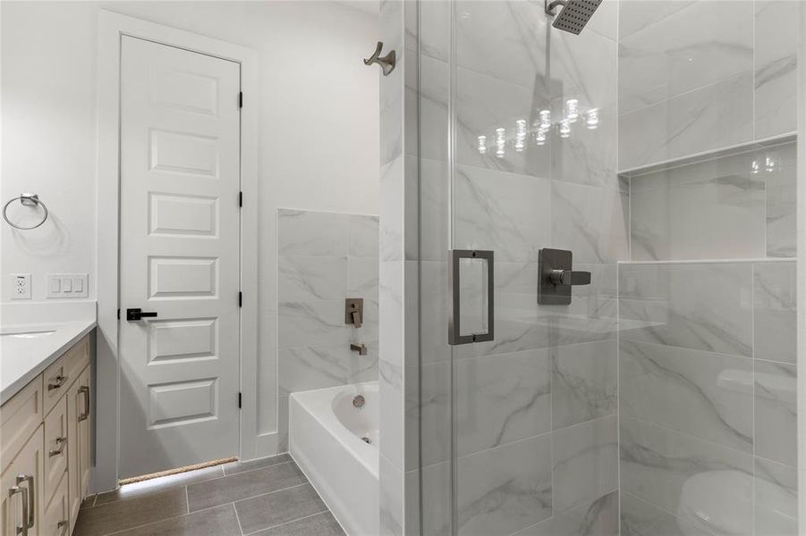 Full bathroom with vanity, a marble finish shower, a garden tub, and dark tile patterned floors Full bathroom with vanity, a marble finish shower, a garden tub, and dark tile patterned floors