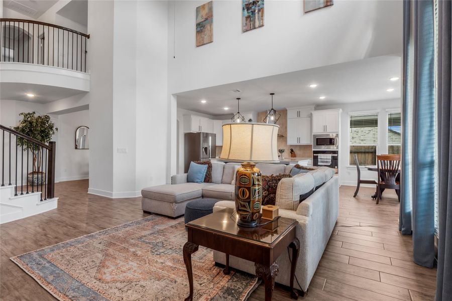 Living area featuring light wood-style flooring, a towering ceiling, stairs, and recessed lighting Living area featuring light wood-style flooring, a towering ceiling, stairs, and recessed lighting