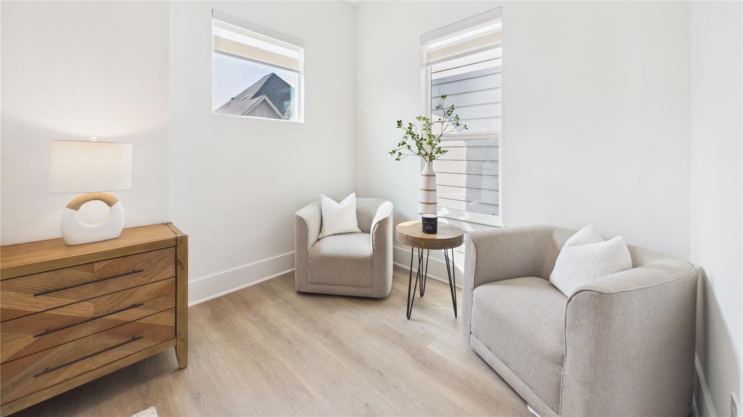 Cozy, bright room with two modern armchairs and a small side table. Features a wooden dresser with a lamp, light wood flooring, and two windows providing natural light. Ideal for a reading nook or small sitting area.