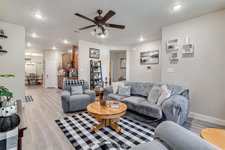 Living room featuring ceiling fan with notable chandelier and light hardwood / wood-style flooring