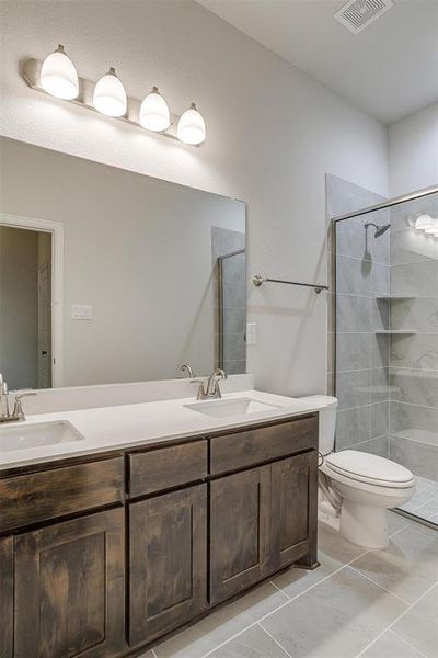 Bathroom featuring tiled shower, vanity, toilet, and tile patterned flooring