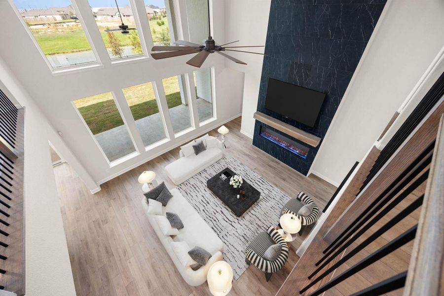 Stunning bird's-eye perspective from the upstairs catwalk, capturing the true scale and layout of the two-story family room. This view emphasizes the dramatic, soaring volume of the space, centered around the floor-to-ceiling dark marble-wrap fireplace. The massive double-tier window wall frames clear views of the backyard and community lake, showcasing how beautifully the home balances grand architectural design with bright, comfortable living. *Virtually Staged Stunning bird's-eye perspective from the upstairs catwalk, capturing the true scale and layout of the two-story family room. This view emphasizes the dramatic, soaring volume of the space, centered around the floor-to-ceiling dark marble-wrap fireplace. The massive double-tier window wall frames clear views of the backyard and community lake, showcasing how beautifully the home balances grand architectural design with bright, comfortable living. *Virtually Staged