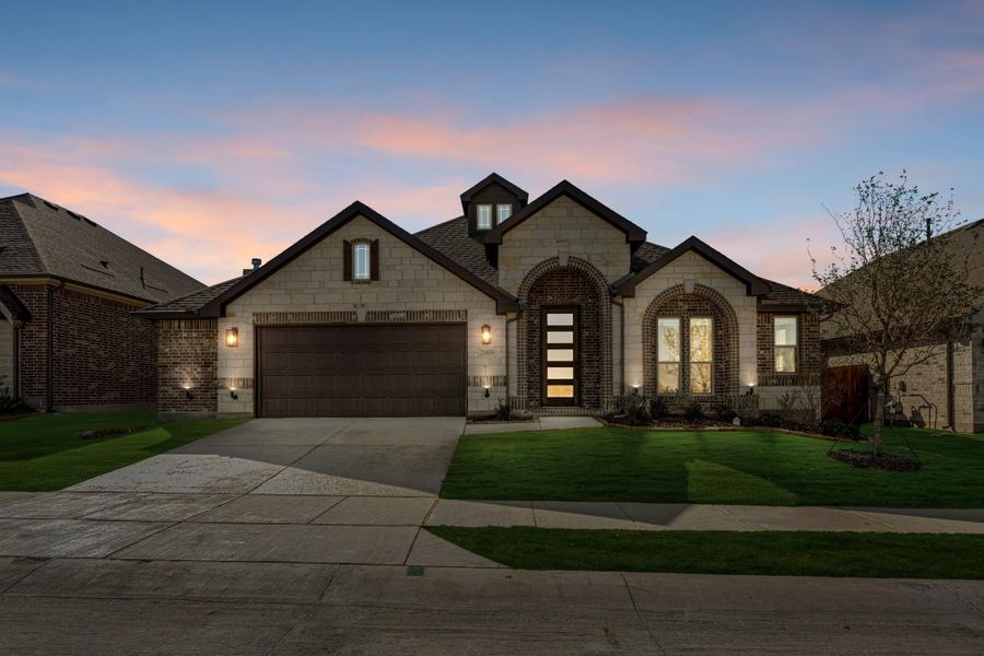 Single-story home with stone and brick exterior, two-car garage, arched entry, and green front lawn at dusk.