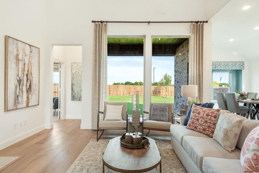 Living room with hardwood floors, large windows, neutral sofa, and accent chairs overlooking a fenced backyard Living room with hardwood floors, large windows, neutral sofa, and accent chairs overlooking a fenced backyard