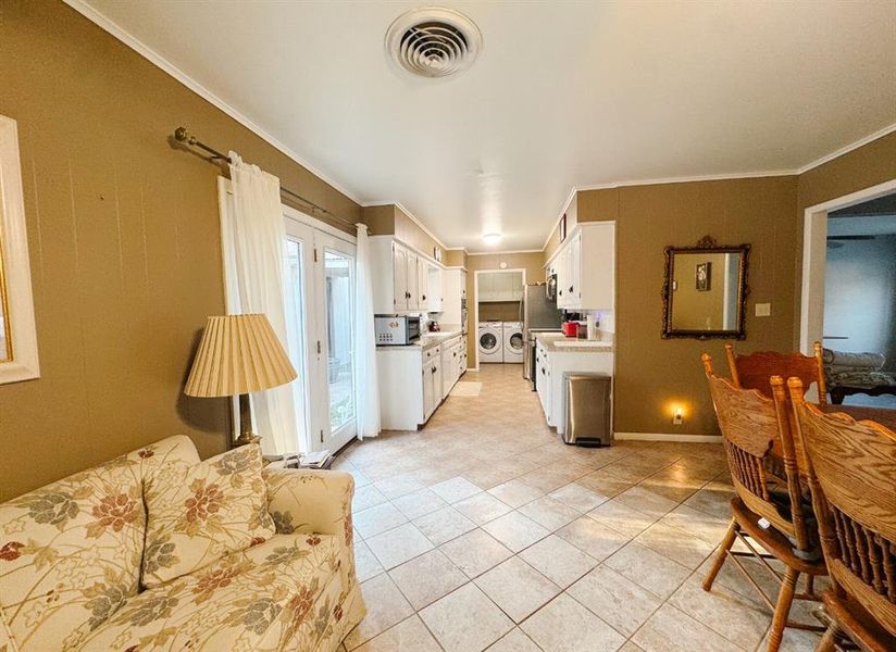 Kitchen with white cabinetry, light countertops, light tile patterned floors, crown molding, and washer and clothes dryer