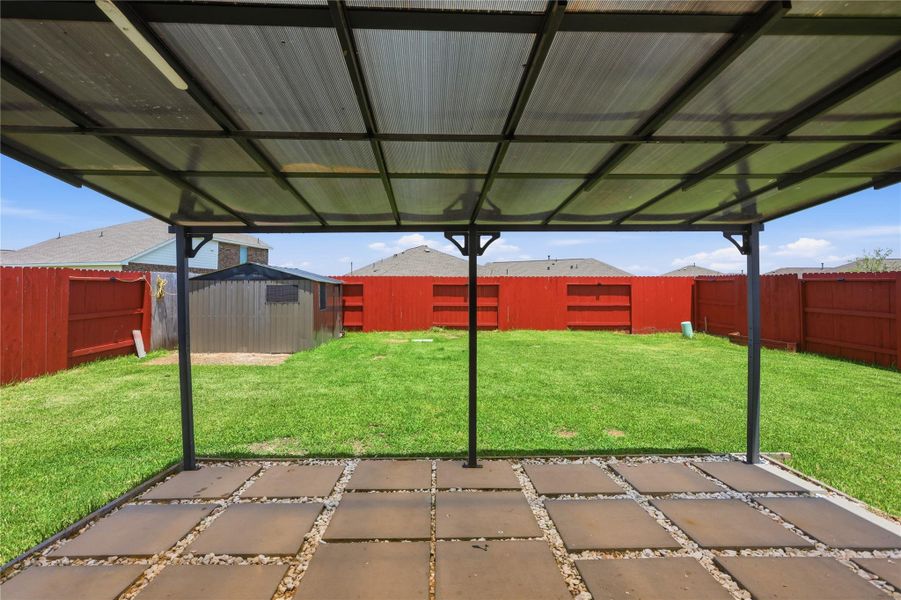 View of the back yard from the back door.  Covered patio structure with concrete pavers.