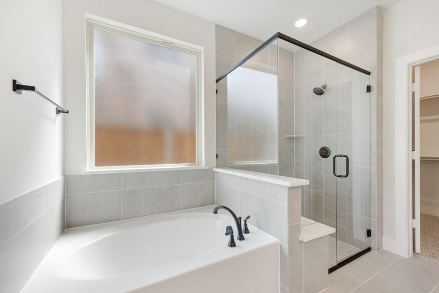 Master bathroom with soaking tub, glass-enclosed shower, gray tile walls, and dark bronze fixtures