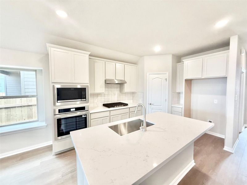 Kitchen with tasteful backsplash, white cabinets, stainless steel appliances, an island with sink, and light wood-style flooring Kitchen with tasteful backsplash, white cabinets, stainless steel appliances, an island with sink, and light wood-style flooring