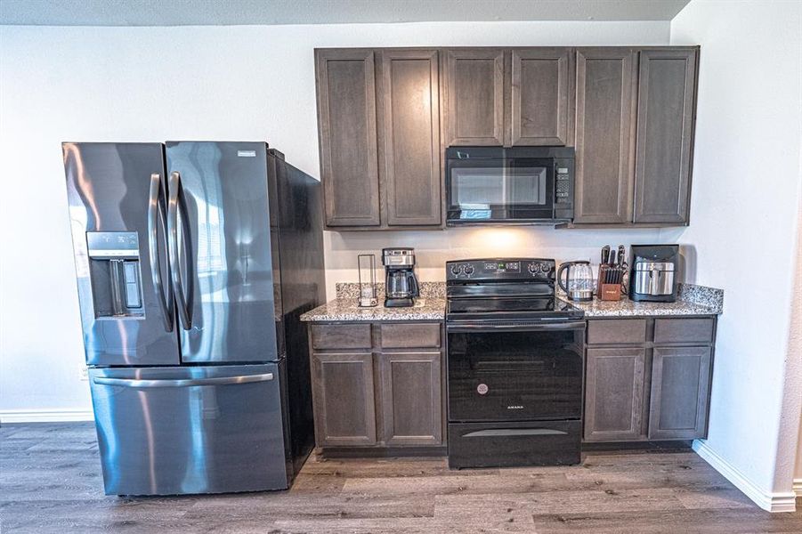 Kitchen featuring dark brown cabinetry, black appliances, light stone counters, and light wood-type flooring