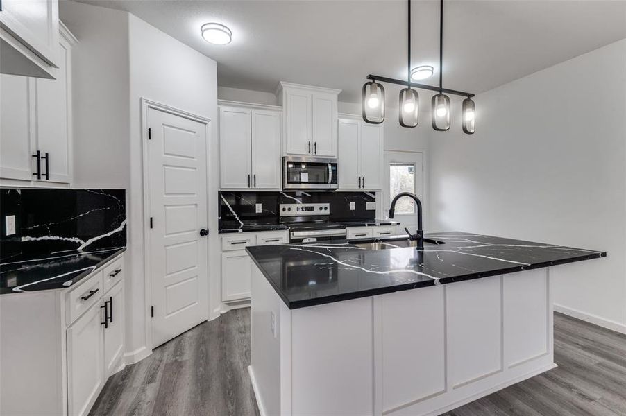 Kitchen with decorative backsplash, stainless steel appliances, white cabinets, and a center island with sink