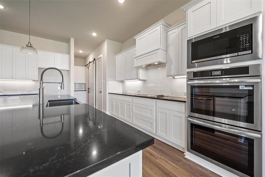 Kitchen with stainless steel appliances, backsplash, white cabinetry, recessed lighting, and pendant lighting Kitchen with stainless steel appliances, backsplash, white cabinetry, recessed lighting, and pendant lighting