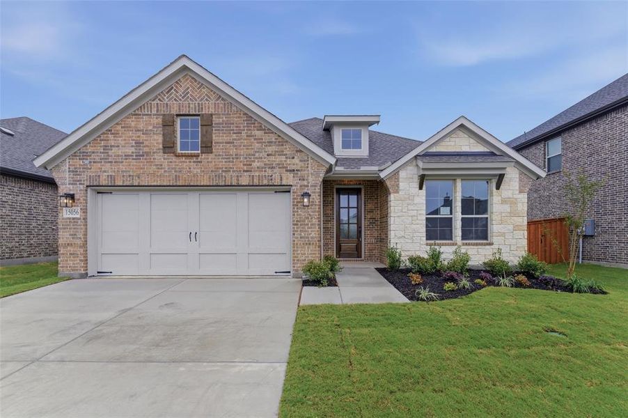 Charming facade featuring a two-car garage, brick and stone exterior, professional landscaping, and a welcoming entryway