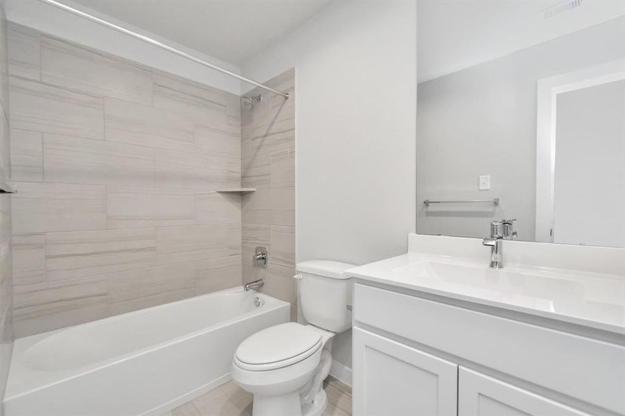 The guest suite bathroom, where elegant flooring complements a tub/shower combo with tile surround. Light wood cabinets complete with a beautiful light countertop, enhances the space for a truly inviting ambiance. Sample photo of completed home with similar floor plan. As-built interior colors and selections may vary.