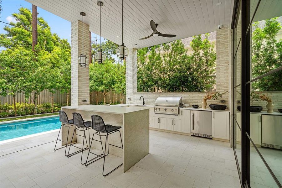 The veranda offers a captivating outdoor haven, featuring a cascading bar countertop, a built-in gas grill with ample storage cabinets beneath, a convenient sink, and a seamlessly integrated mini-fridge. This exquisite setup creates the perfect entertainment space for any gathering.