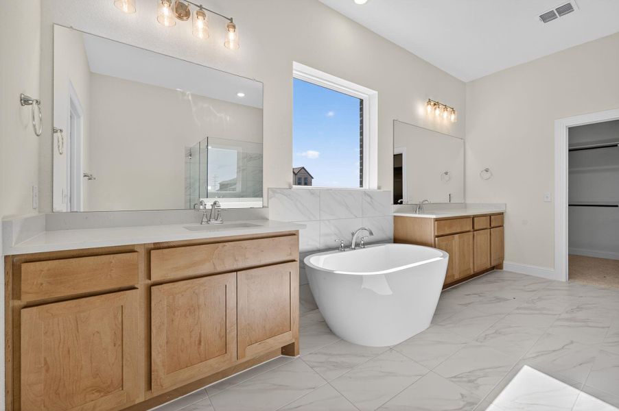 Full bathroom with light marble finish floors, a freestanding tub, two vanities, and a marble finish shower